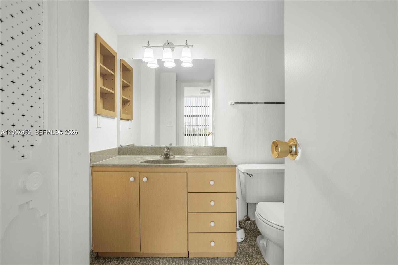 Bathroom vanity featuring light wood-finish cabinetry, stone-style countertop, inset sink, large rectangular wall mirror, and built-in recessed shelving