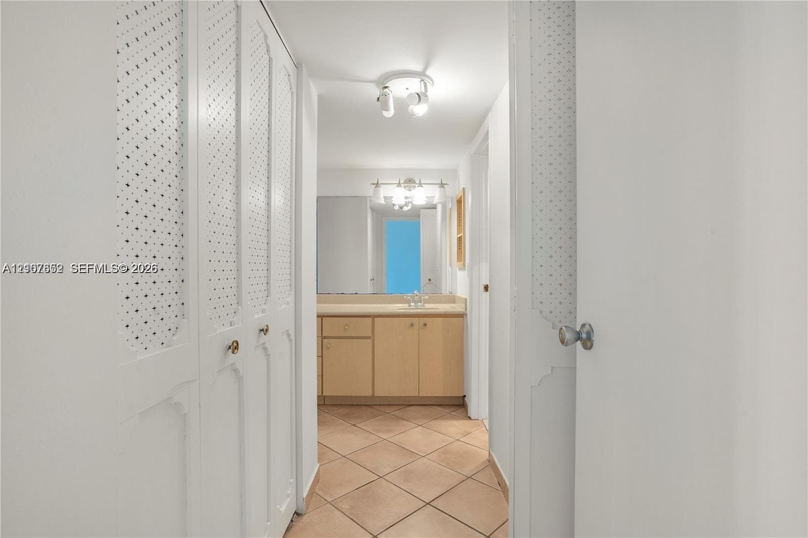 Bathroom interior featuring wood-finish cabinetry, tile flooring, built-in storage closets with decorative metal grille inserts, and a dual-bulb vanity light fixture