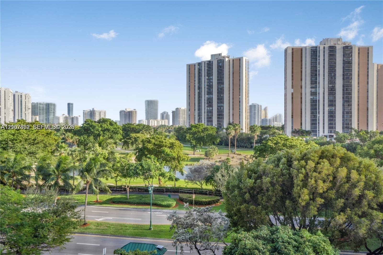 Panoramic perspective featuring expansive green spaces, mature trees, a central body of water, and an urban skyline