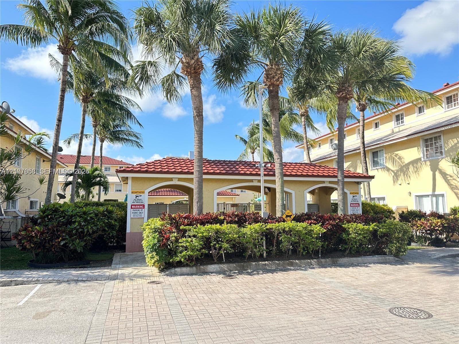 Community pavilion featuring a terracotta tile roof, arched architectural details, paved hardscaping, and mature palm landscaping