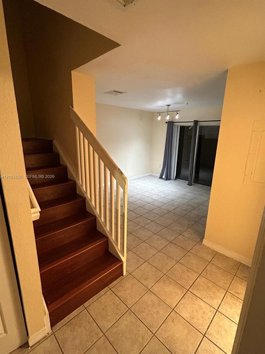 Staircase with wood-finish treads, white railing, ceramic tile flooring, and multi-bulb light fixture