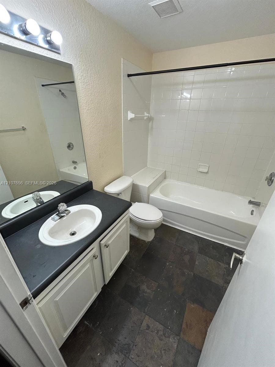 Bathroom featuring a vanity with dark countertop and inset oval sink, white cabinetry, tile flooring, and a tub-shower combination with full-height tile surround