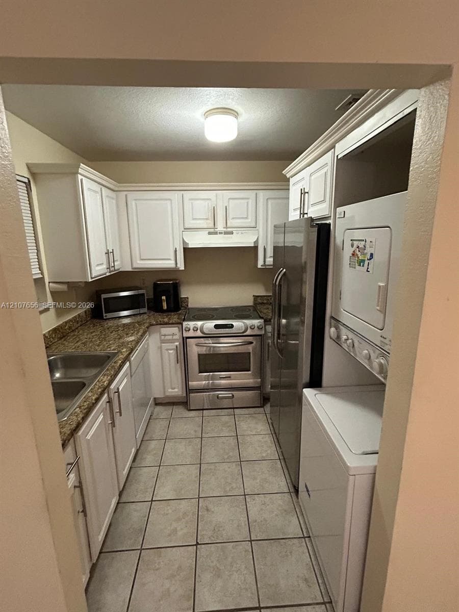 Kitchen featuring white shaker-style cabinetry, stone-finish countertops, stainless steel appliances, tile flooring, and integrated laundry appliances