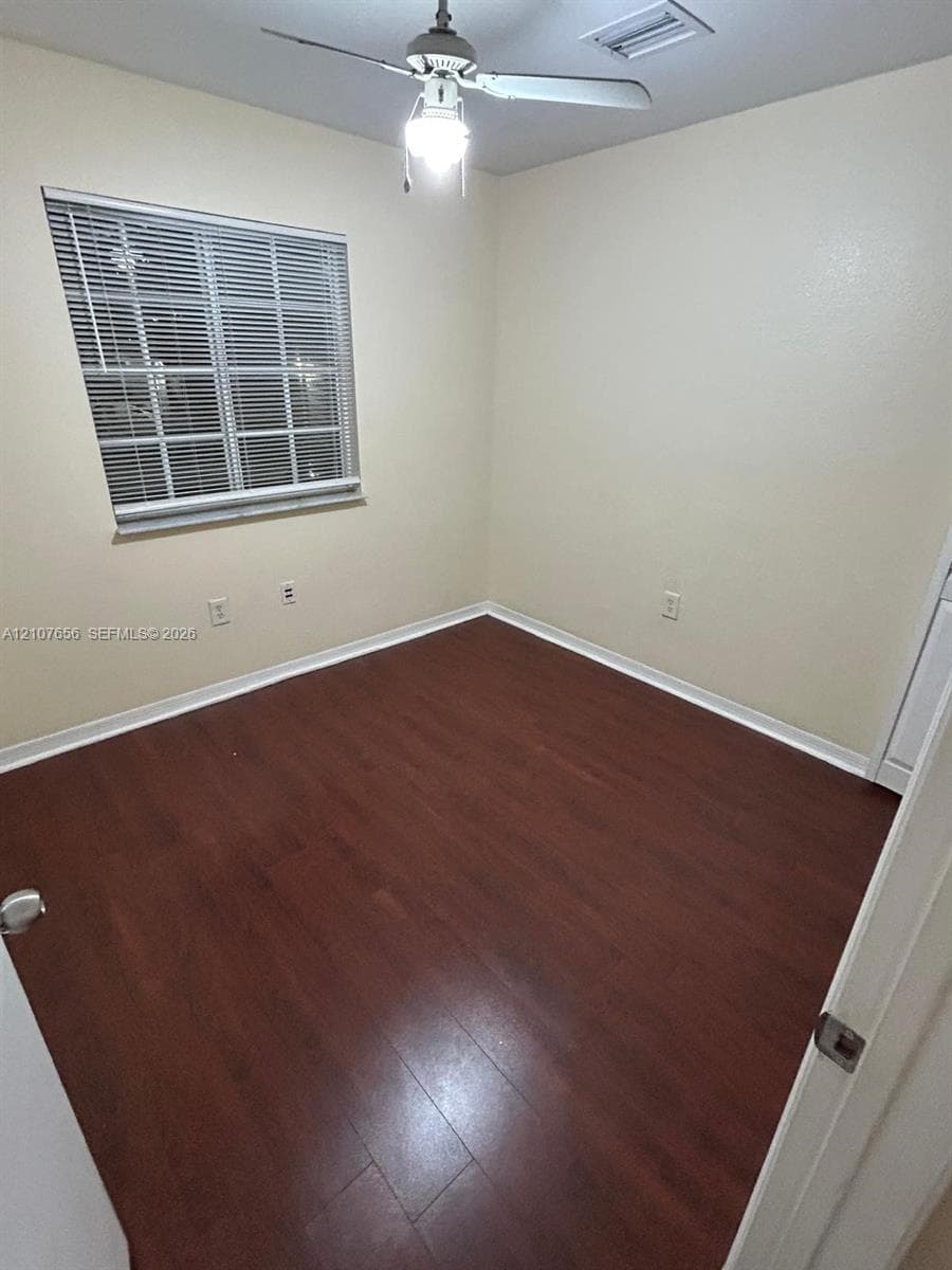 Interior room featuring wood-finish flooring, a ceiling fan with integrated light fixture, and a window with horizontal blinds