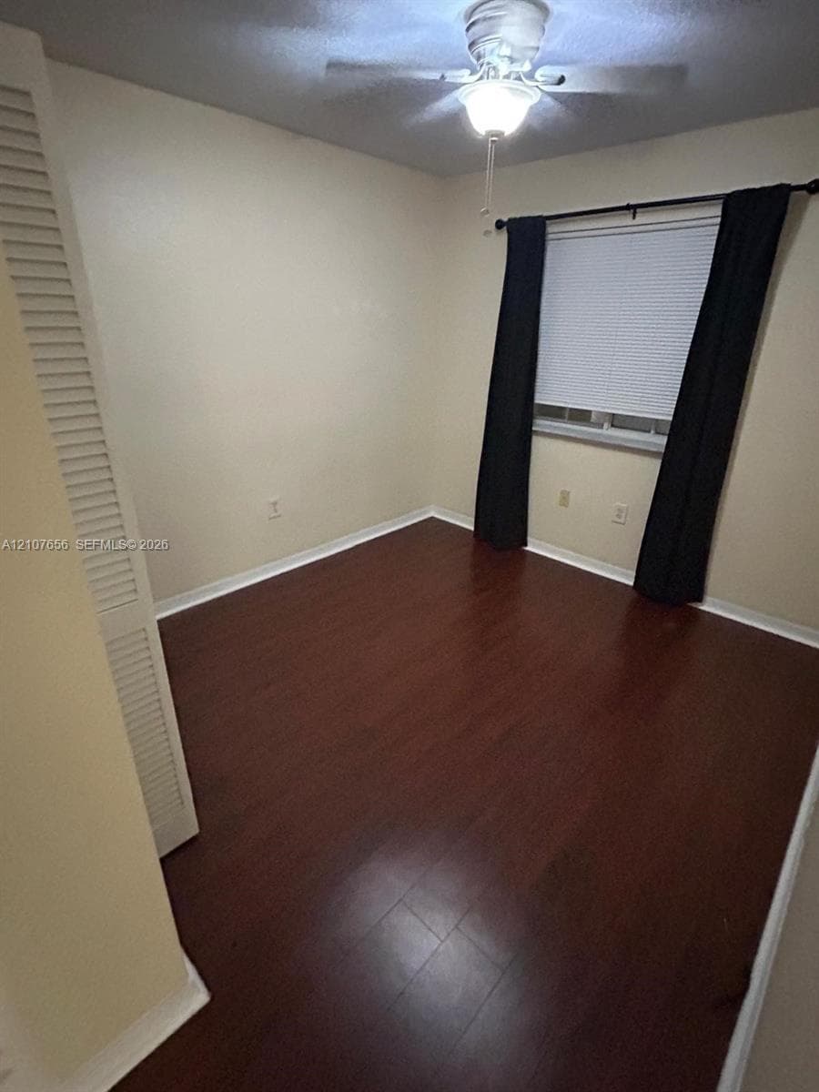 Room interior featuring wood-finish flooring, a ceiling fan with integrated lighting, and a closet with louvered bi-fold doors