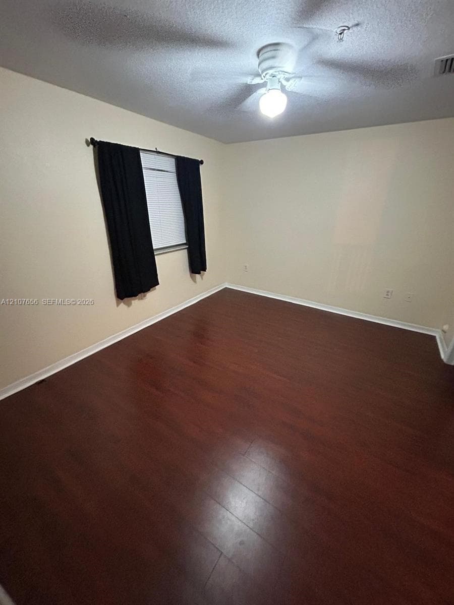 Interior space featuring dark wood-finish flooring, neutral wall tones, and a ceiling-mounted light fixture with an integrated fan