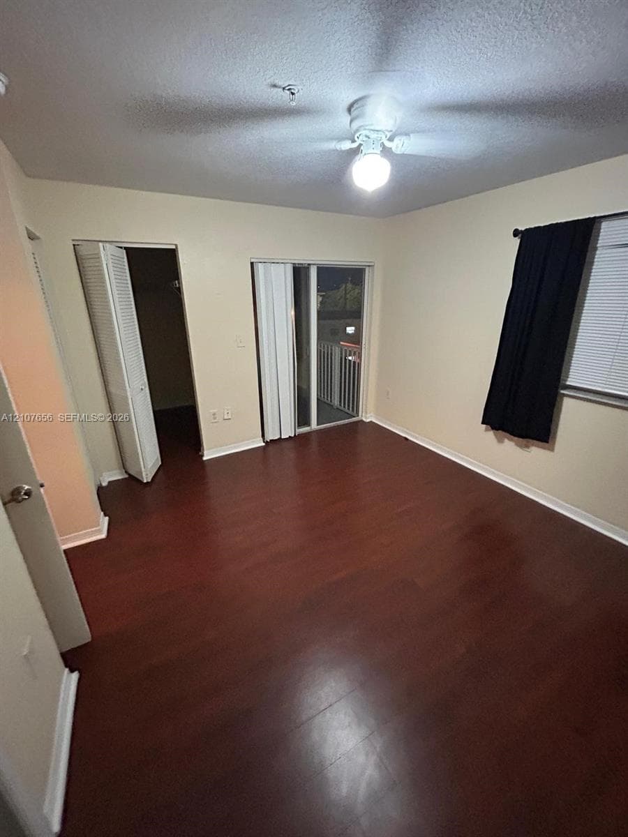 Wood-finish flooring, sliding glass door with balcony access, ceiling fan with light fixture, and closet with louvered doors