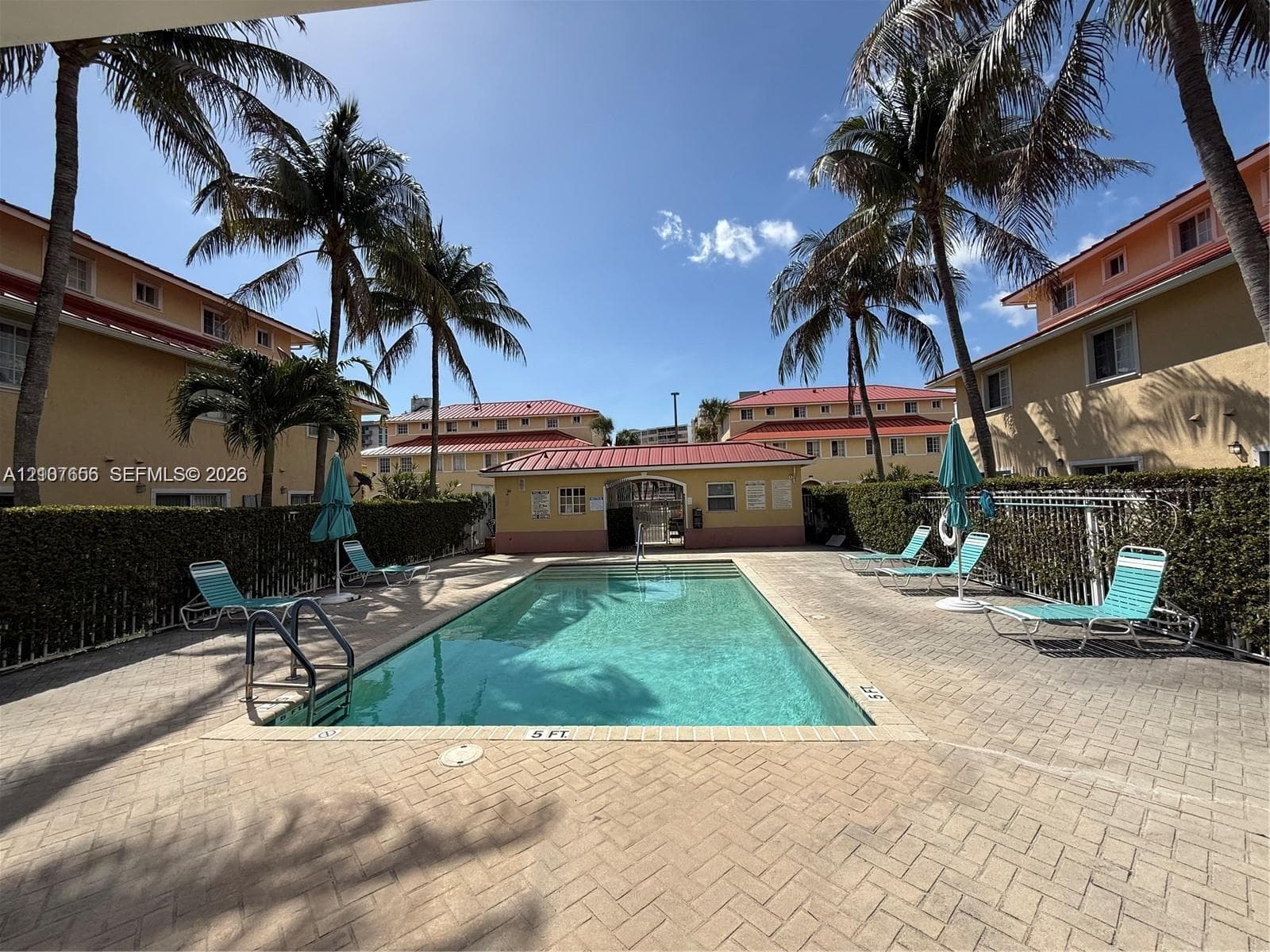 Outdoor swimming pool featuring a brick-paved deck, perimeter metal fencing, and mature palm trees