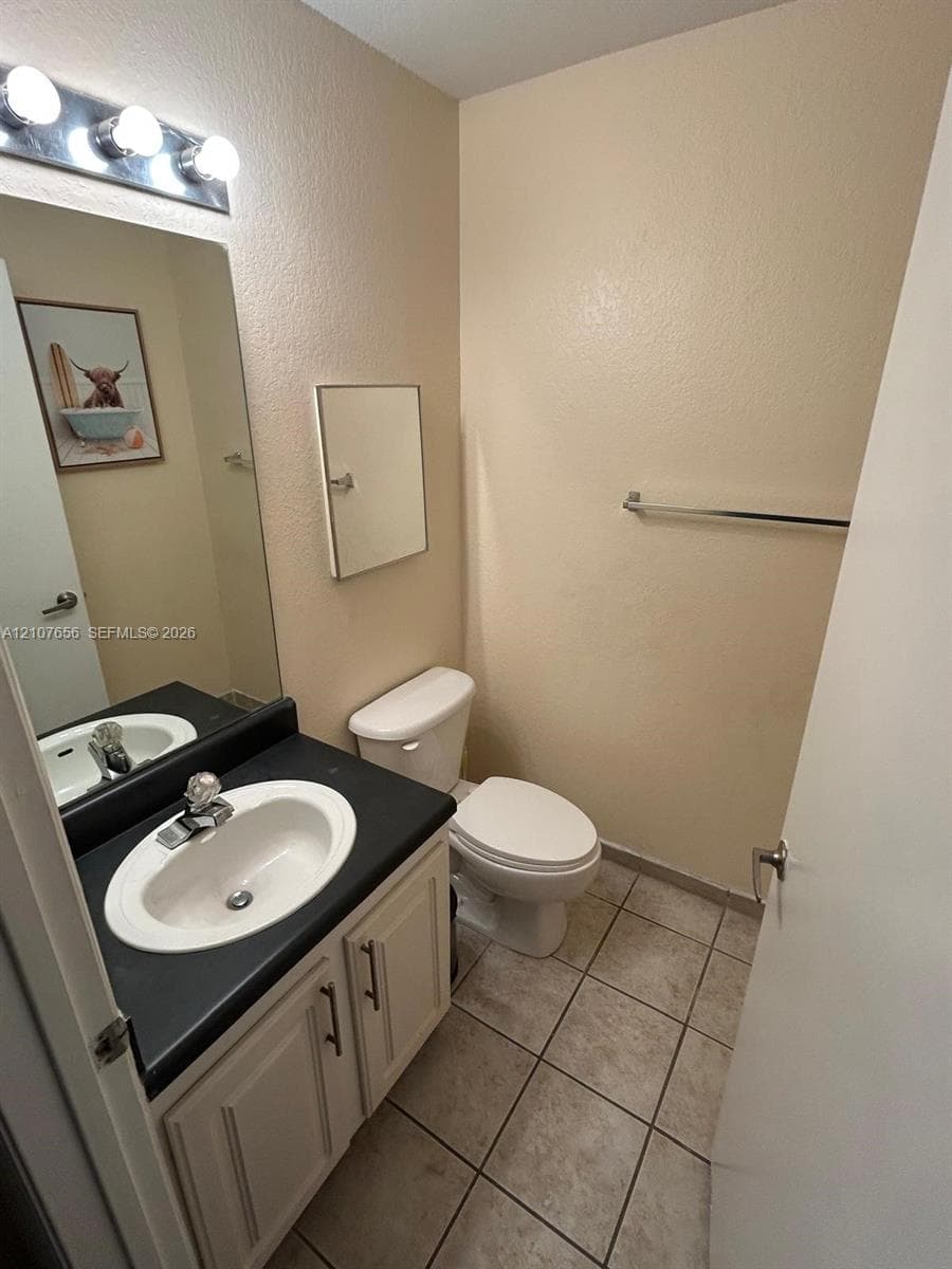 Bathroom featuring a vanity with dark countertop, integrated oval sink, ceramic tile flooring, and a multi-bulb vanity light fixture