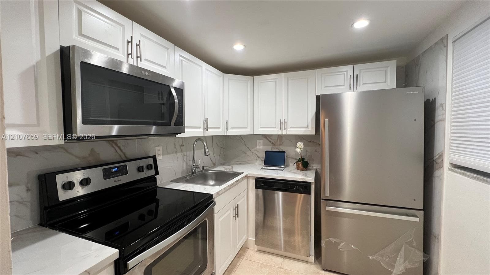 Kitchen featuring white shaker-style cabinetry, stainless steel appliances, stone-finish countertops, full-height decorative backsplash, and recessed lighting