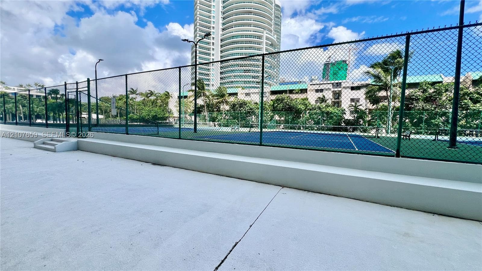 Tennis courts enclosed by chain-link fencing featuring concrete surround, perimeter lighting, and stepped platforms