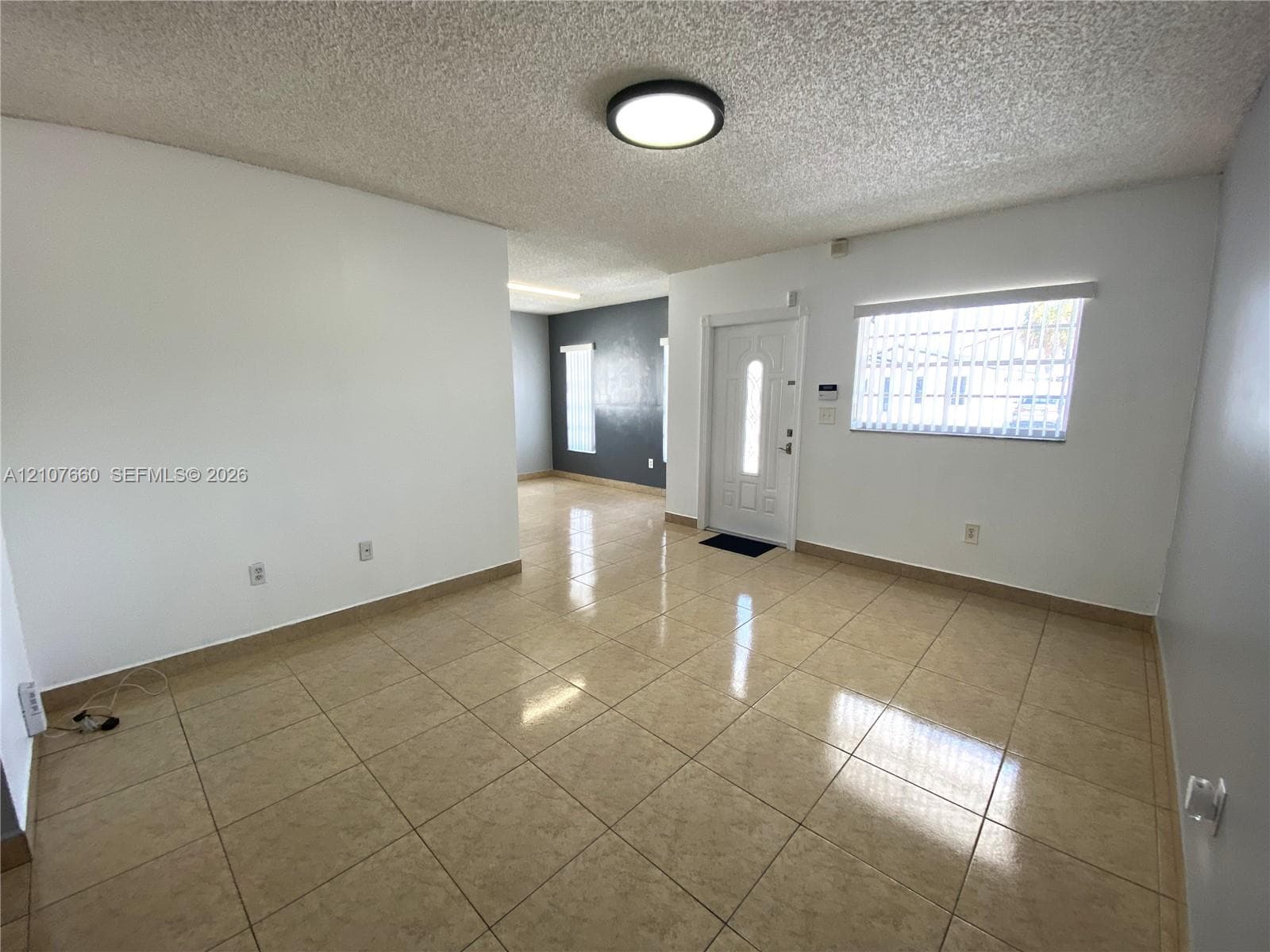 Interior space featuring neutral-toned tile flooring, recessed flush-mount ceiling lighting, textured ceiling finish, and an exterior door with decorative glass paneling