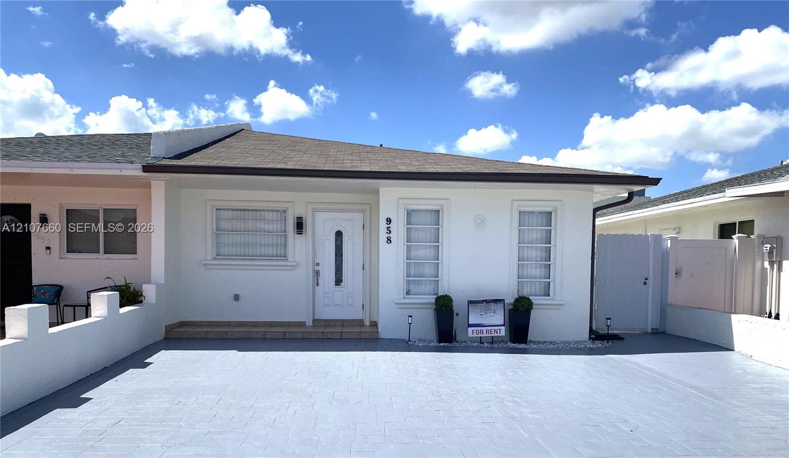 Stucco exterior featuring a paved driveway, low-profile concrete perimeter wall, and single-entry door with glass insert