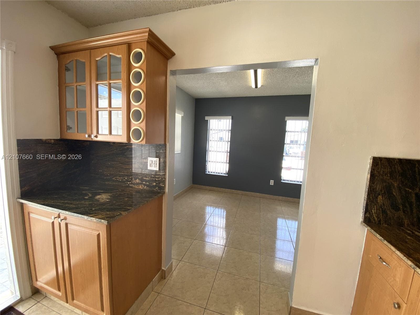 Custom cabinetry featuring glass-panel upper doors and built-in circular wine storage, stone countertops, and polished tile flooring