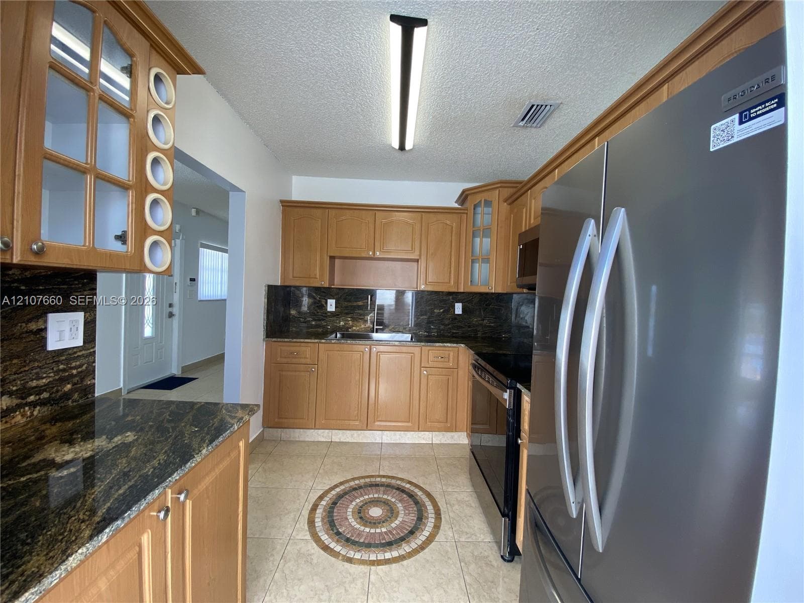 Kitchen featuring natural wood cabinetry, stone countertops, stainless steel refrigerator, electric range, and tiled flooring with a decorative mosaic inlay