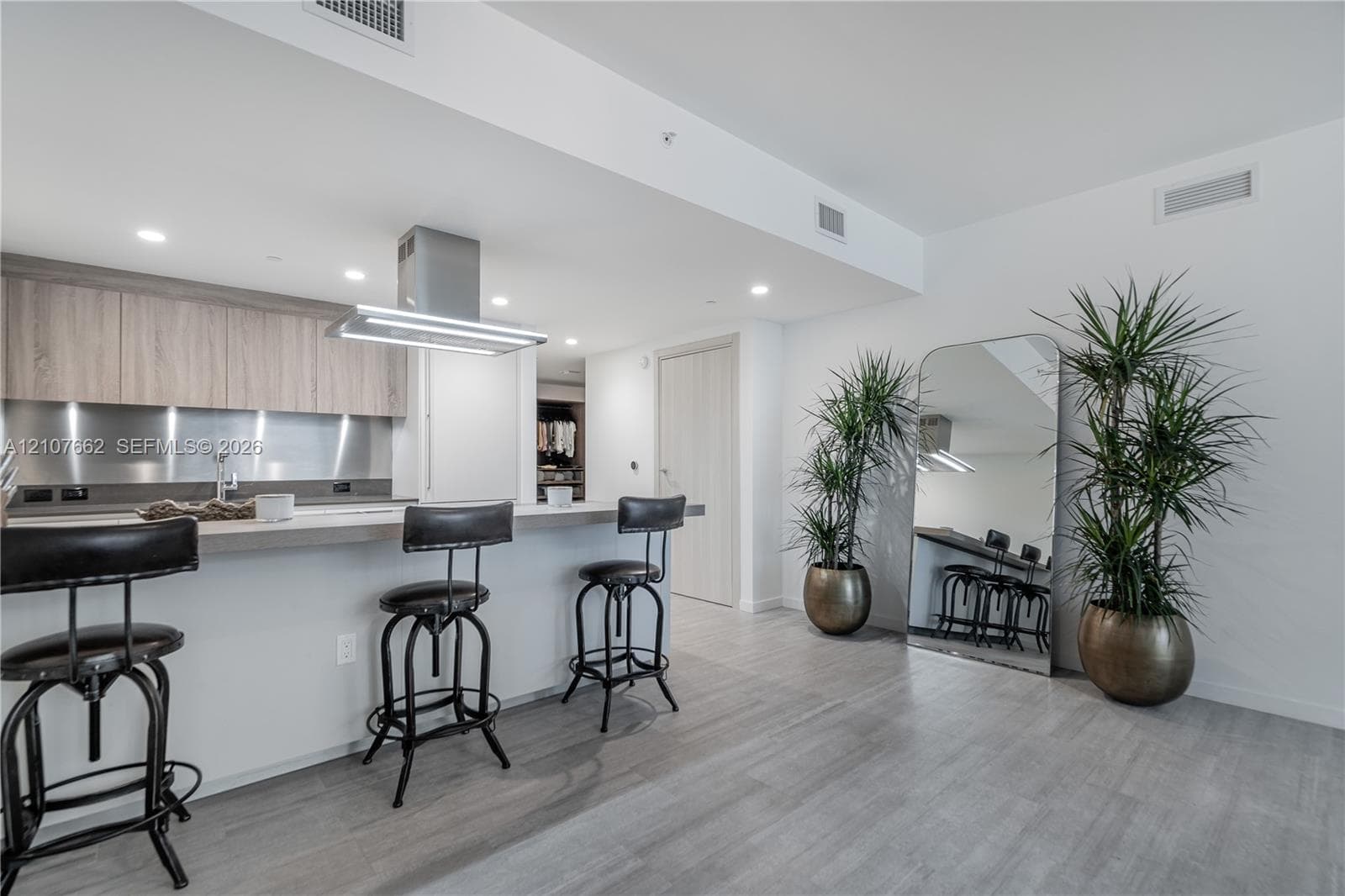 Kitchen featuring wood-finish cabinetry, stainless steel backsplash, stone-top breakfast bar, stainless steel vent hood, and wood-finish flooring