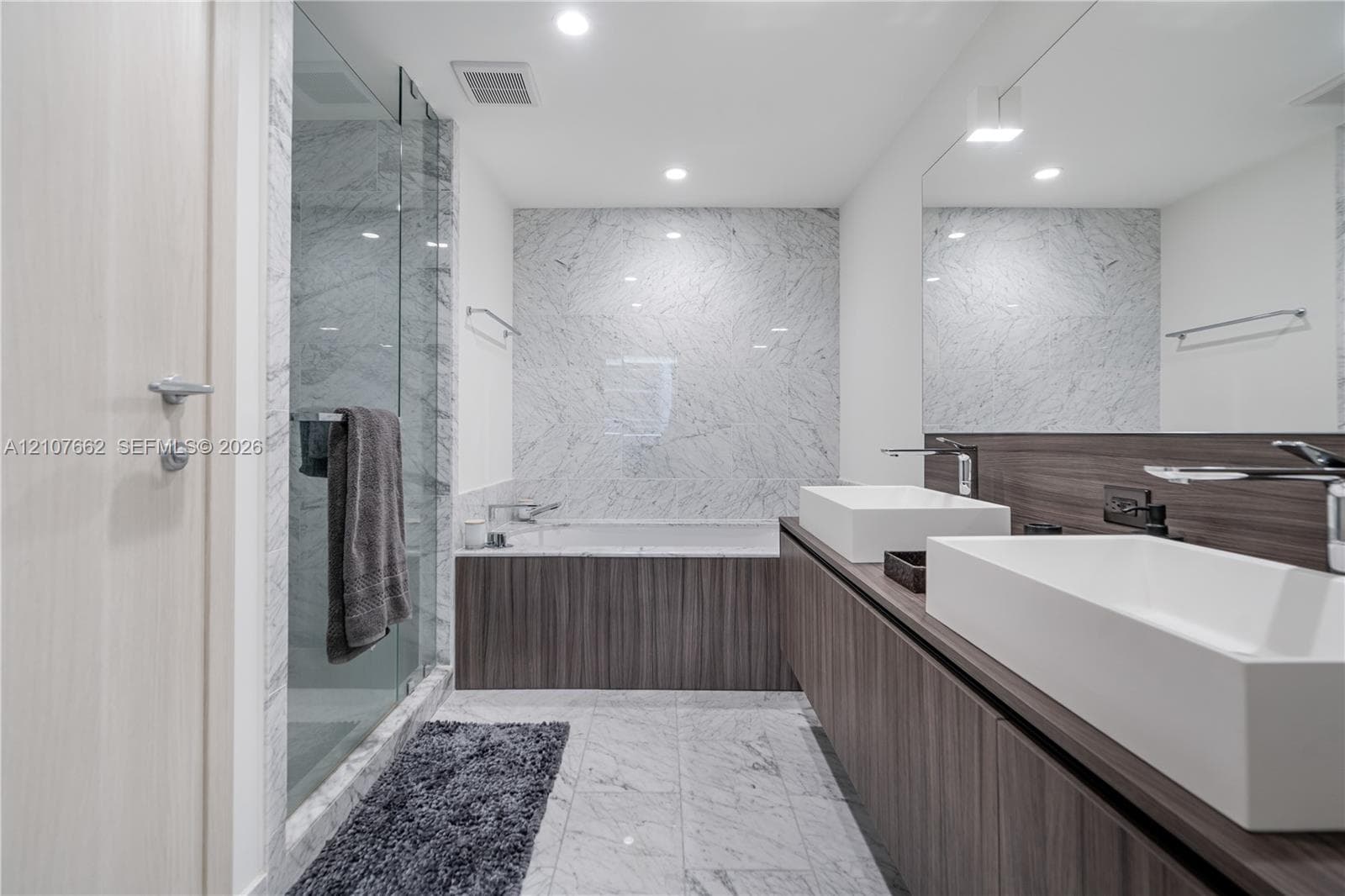 Dual vanity featuring rectangular vessel sinks, dark wood-finish cabinetry, a large wall-mounted mirror, a glass-enclosed shower, and stone-finish wall and floor tile