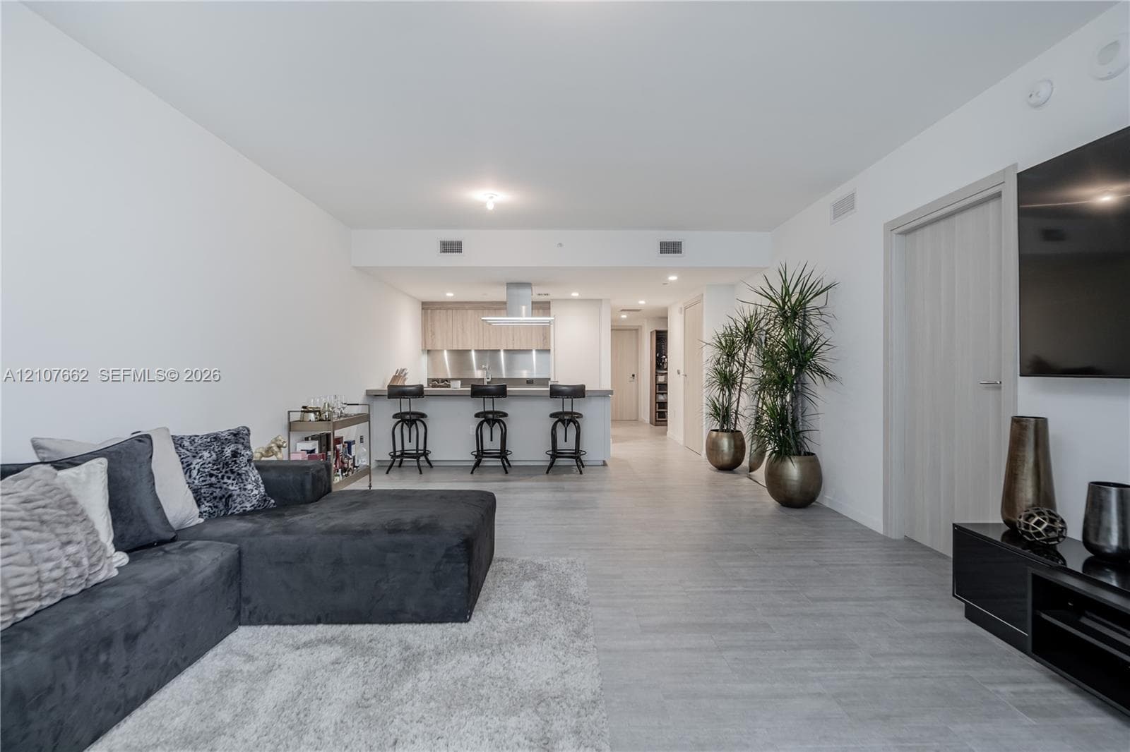 Open-concept interior featuring light wood-finish flooring, a kitchen breakfast bar, neutral-toned slab-front cabinetry, and a modern stainless steel range hood