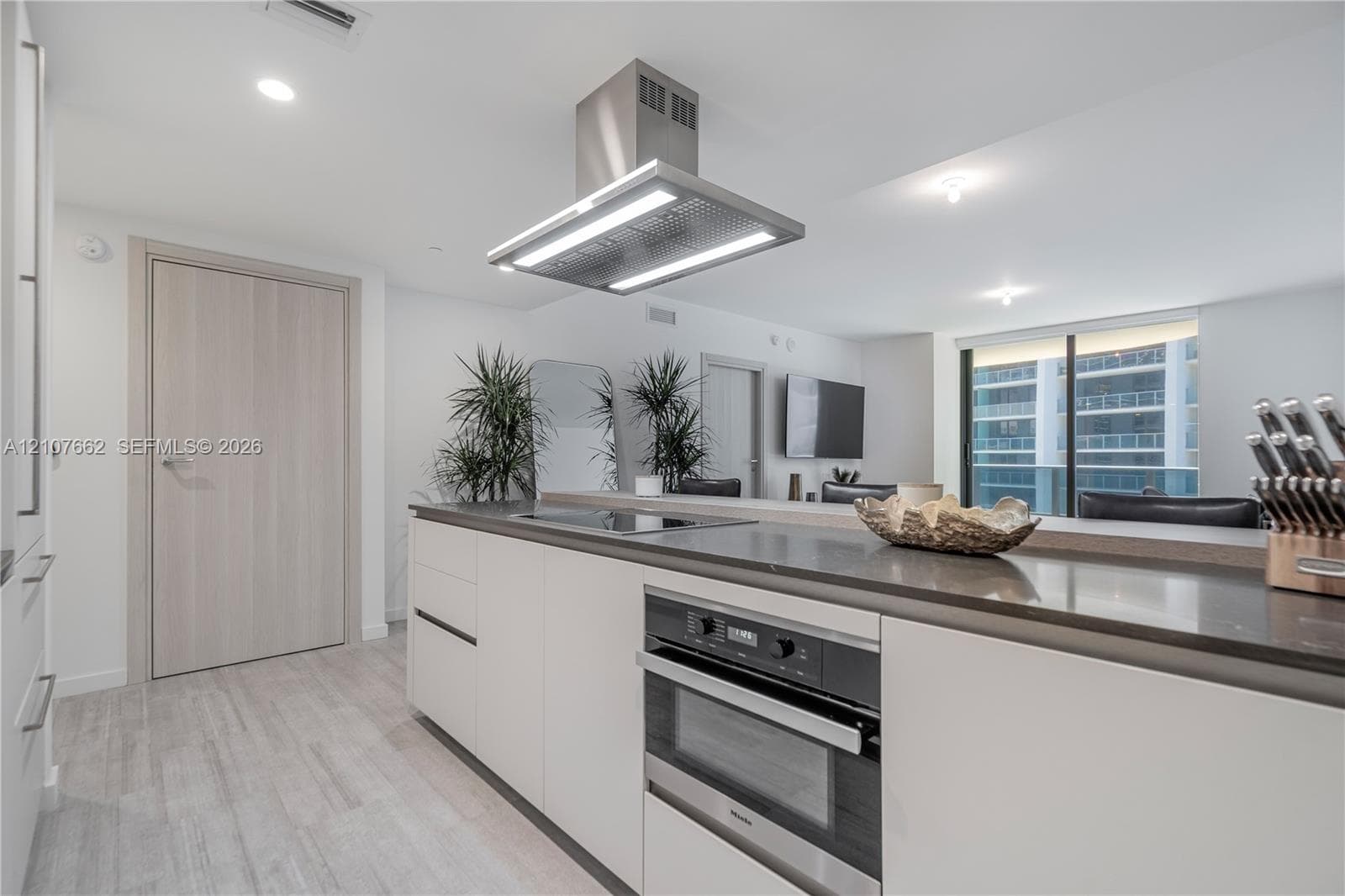 Kitchen featuring a central island with a solid-surface countertop, integrated stainless steel oven, recessed lighting, and a stainless steel ceiling-mounted range hood, complemented by light-toned wood-finish flooring