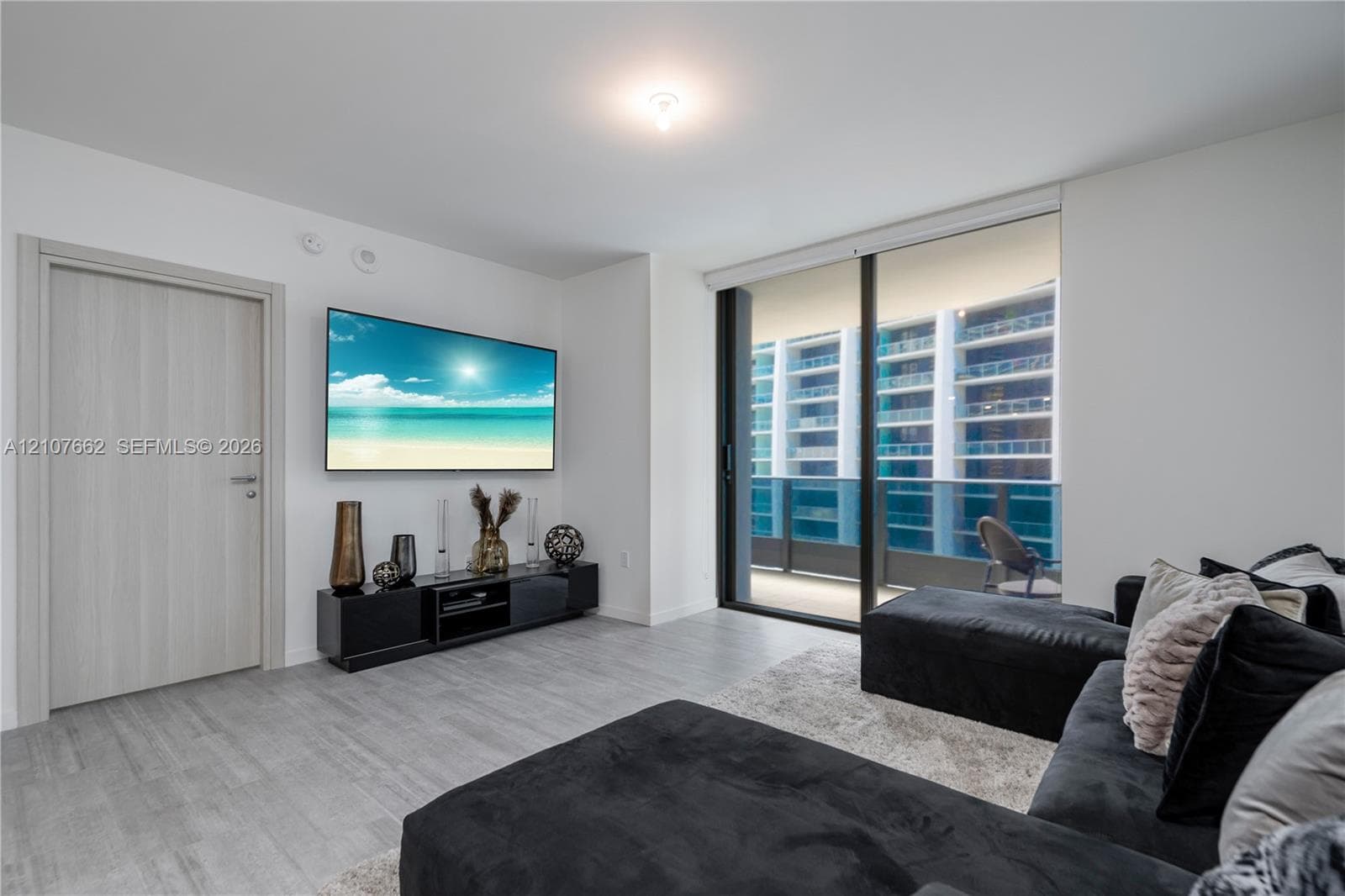 Living area featuring wood-finish flooring, full-height sliding glass doors, and a neutral color palette