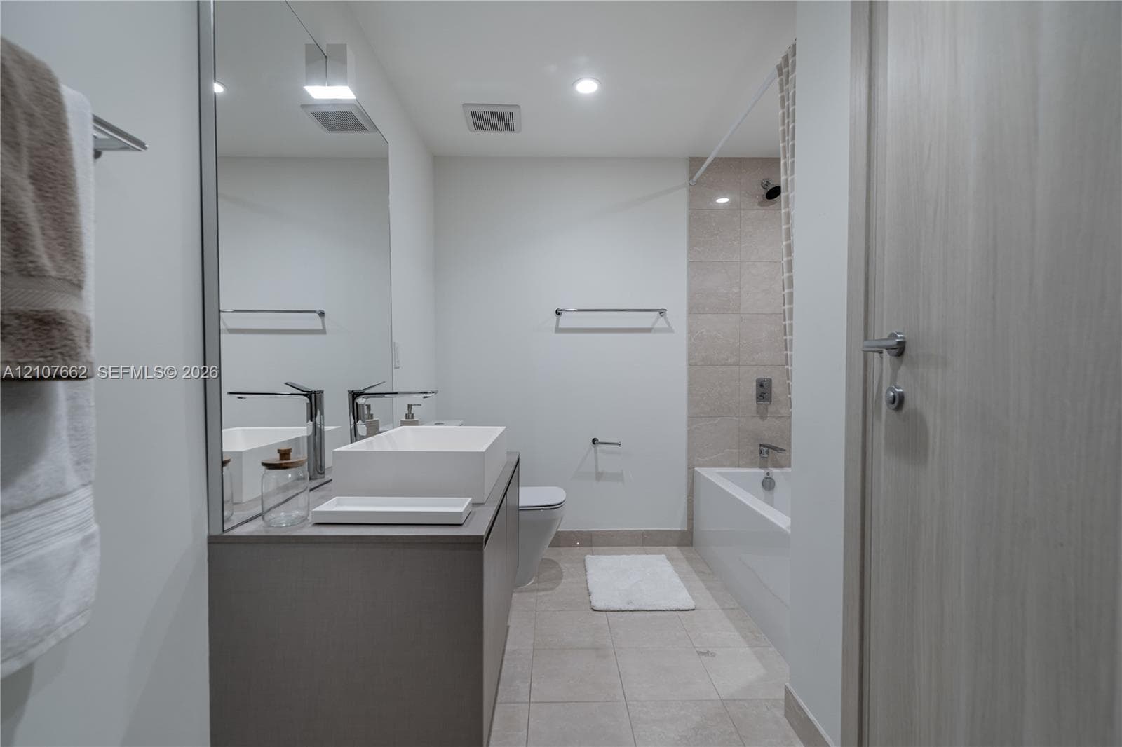 Modern bathroom featuring a floating vanity with a rectangular vessel sink, polished chrome faucet, large wall-mounted mirror, and tile-surround bathtub