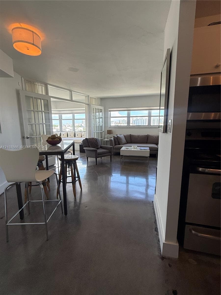 Open-concept floor plan featuring polished concrete flooring, multi-pane French doors, expansive windows with exterior scenery, and integrated stainless steel kitchen appliances