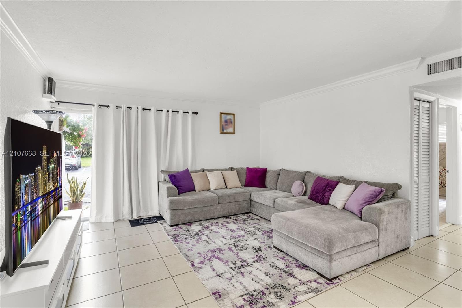 Living space featuring neutral ceramic tile flooring, crown molding, and louvered closet doors