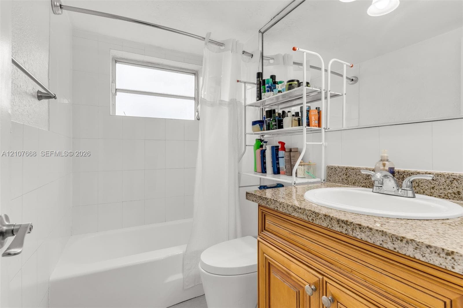 Bathroom featuring a wood-finish vanity with a stone-composite countertop, integrated oval basin, white wall tile surround, and an oversized vanity mirror
