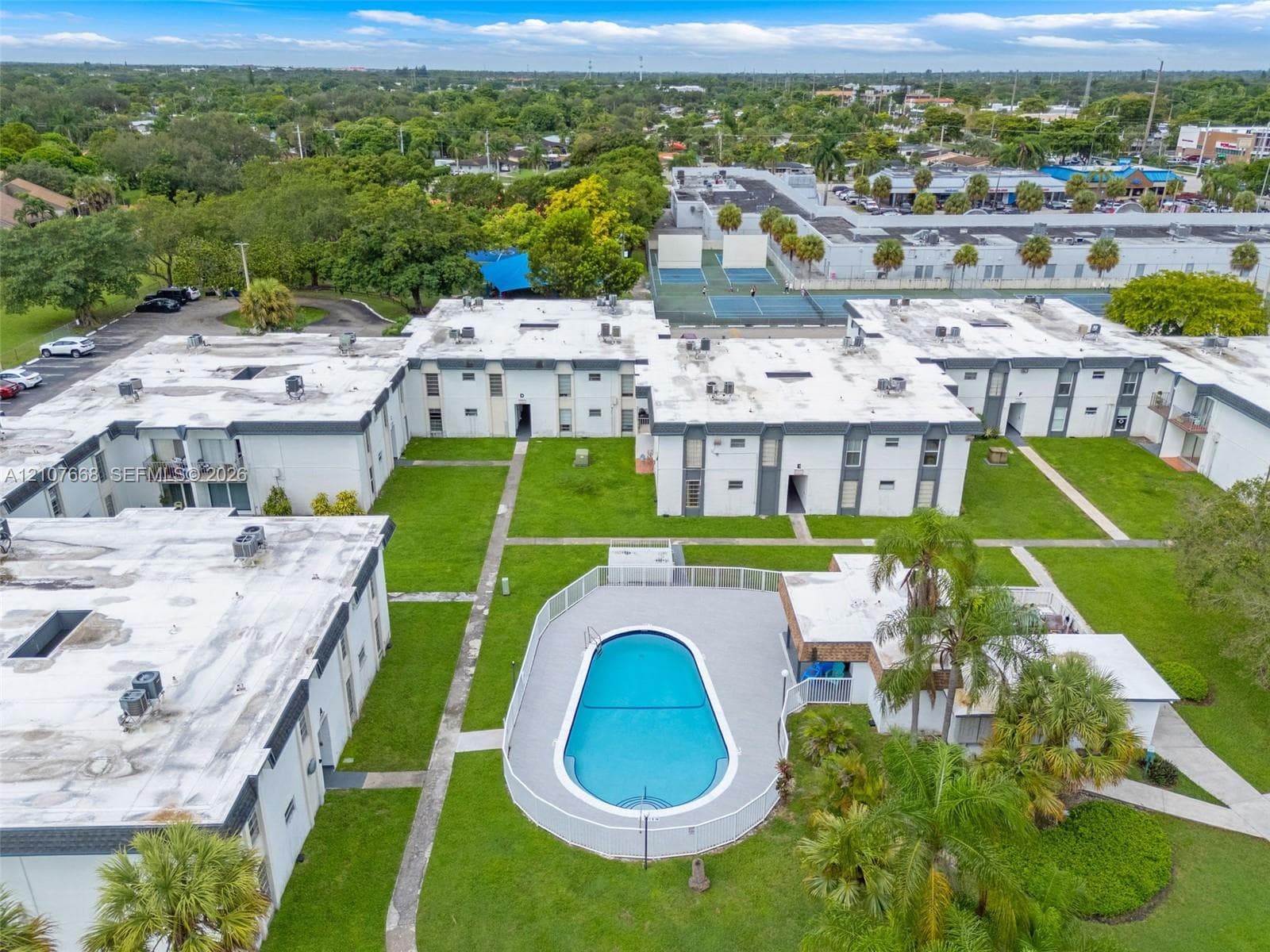 Aerial perspective of the multi-unit complex featuring an outdoor swimming pool with surround decking, mature palms, manicured lawns, and paved walkways