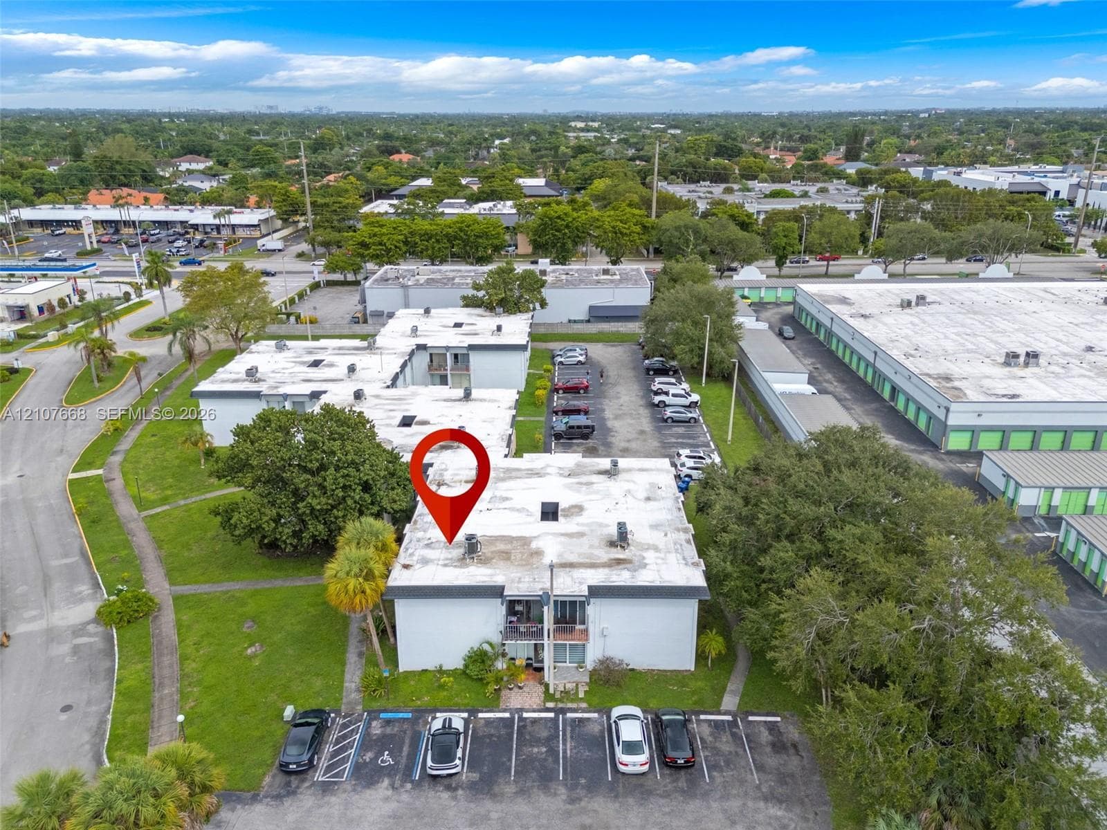 Aerial perspective of a multi-unit property featuring flat roof construction, designated asphalt parking, ground-level landscaping, and mature palm trees