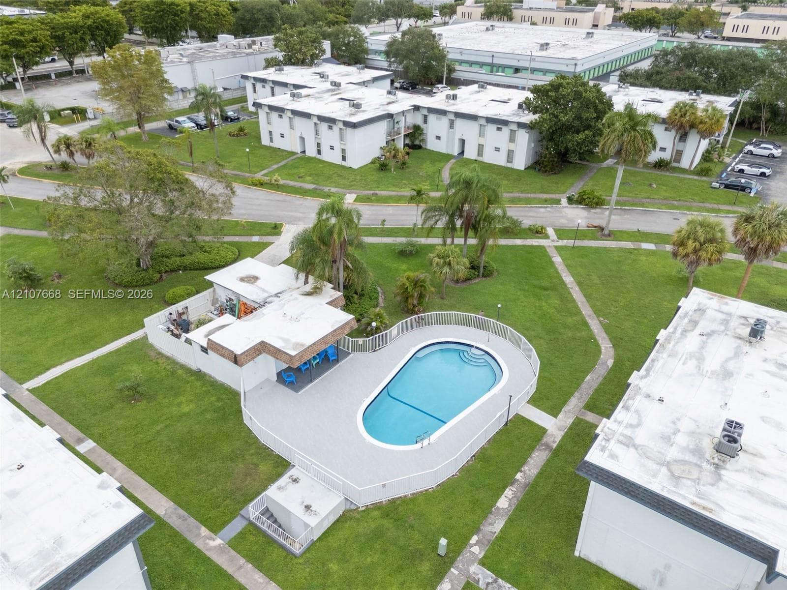 Swimming pool with surrounding paver deck, white perimeter fencing, and covered cabana area situated within expansive landscaped grounds