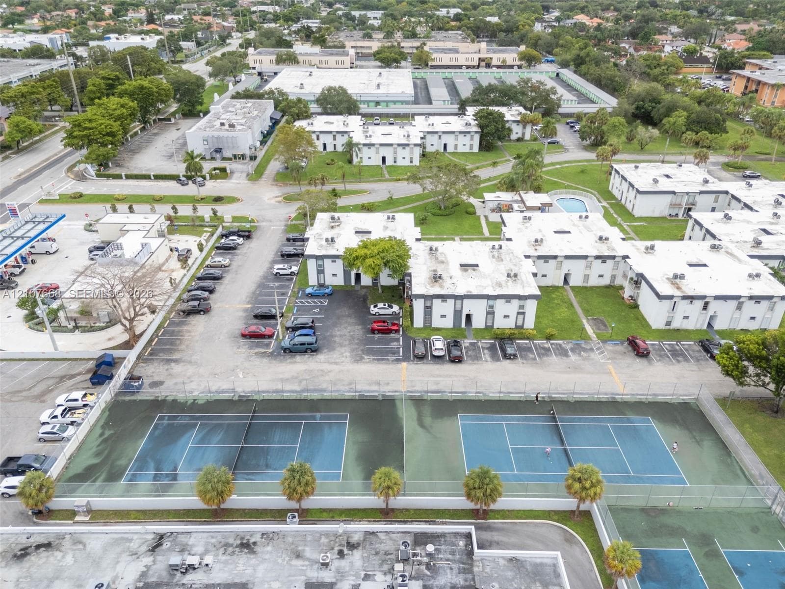 Aerial perspective of residential complex featuring multiple tennis courts, dedicated asphalt parking, and landscaped green space