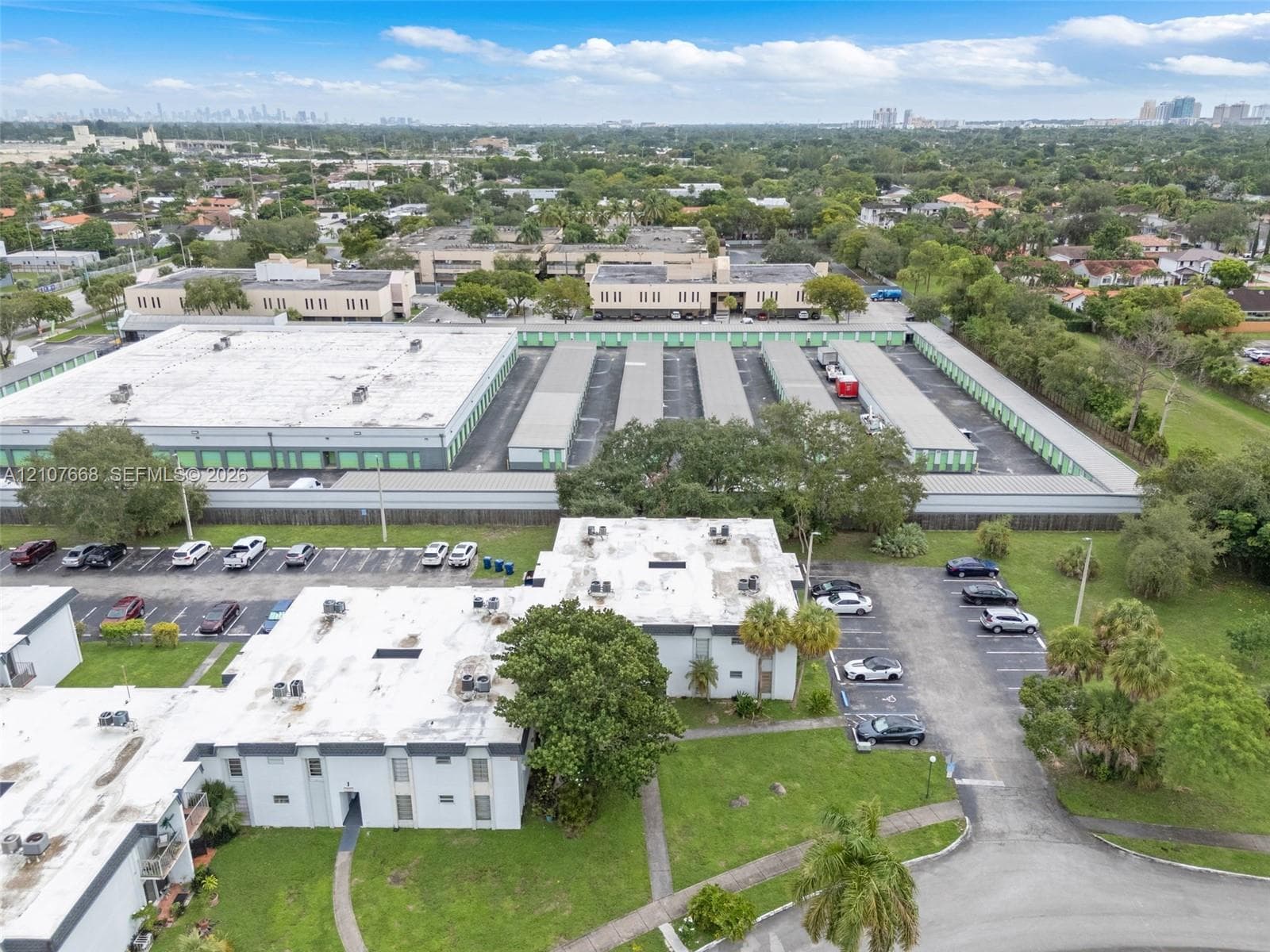 Aerial view of commercial property featuring paved parking areas, multi-unit flat-roof structures, and maintained landscape surroundings