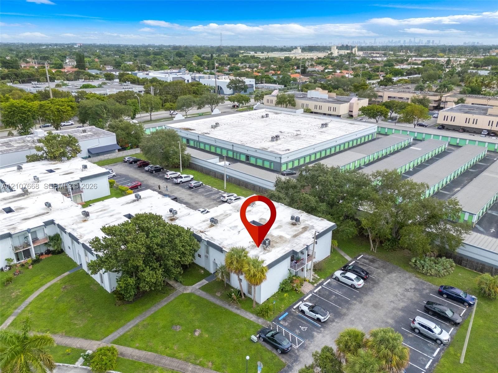 Aerial perspective of a multi-unit property featuring flat roofing, dedicated asphalt parking, integrated exterior lighting, and landscaped green space