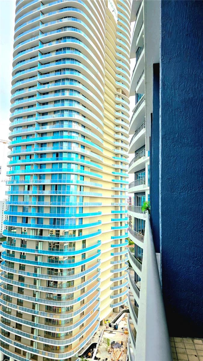 High-rise building exterior featuring a curvilinear concrete facade, floor-to-ceiling glass paneling, and stacked cantilevered balconies