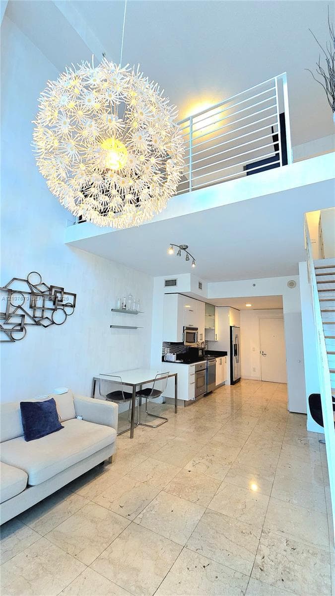 High-ceiling interior featuring stone tile flooring, a statement spherical pendant fixture, a mezzanine level with metal railings, and built-in kitchen cabinetry