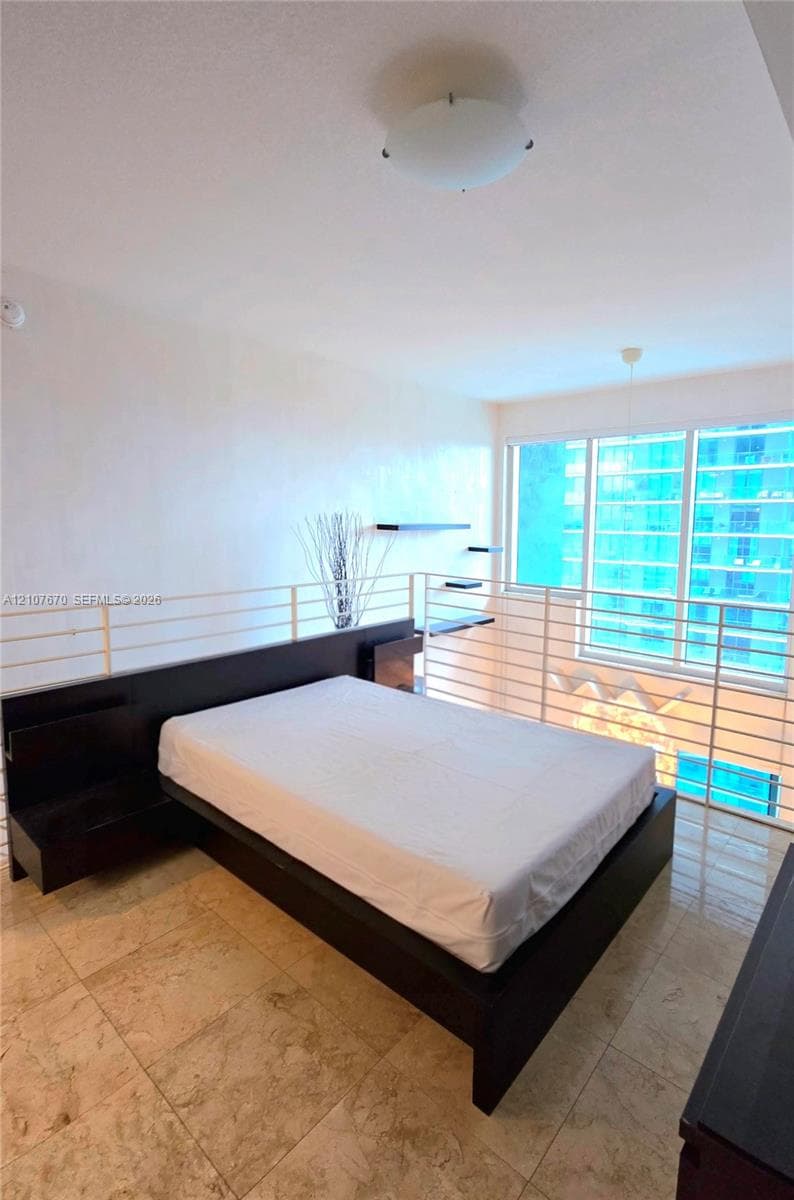 Stone tile flooring, custom dark-finish built-in bed frame with integrated shelving, floating wall shelves, and floor-to-ceiling windows with metal railing
