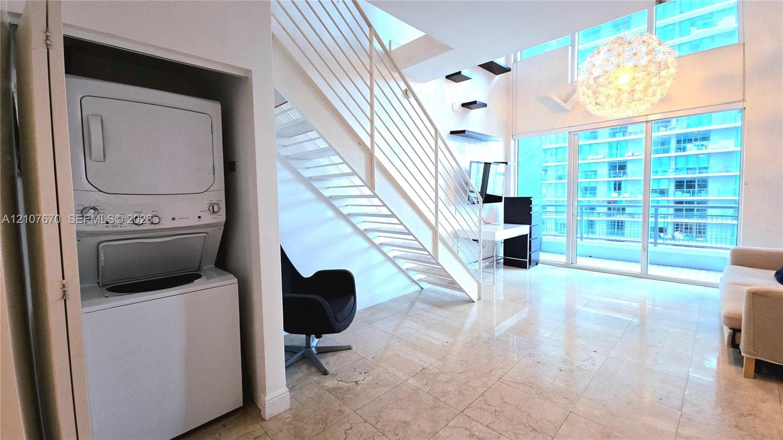 Open-concept interior featuring full-height windows, stone tile flooring, metal staircase with railing, and built-in laundry closet