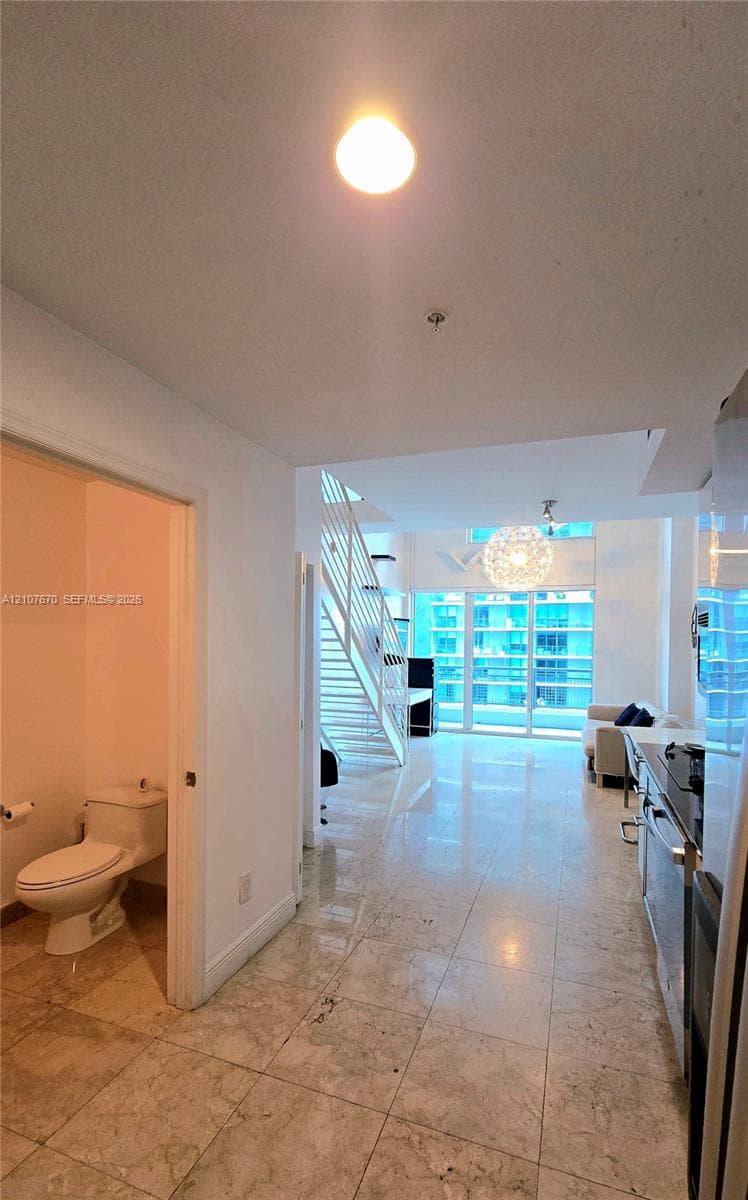 Stone tile flooring, open staircase with white metal railings, floor-to-ceiling windows, and recessed lighting