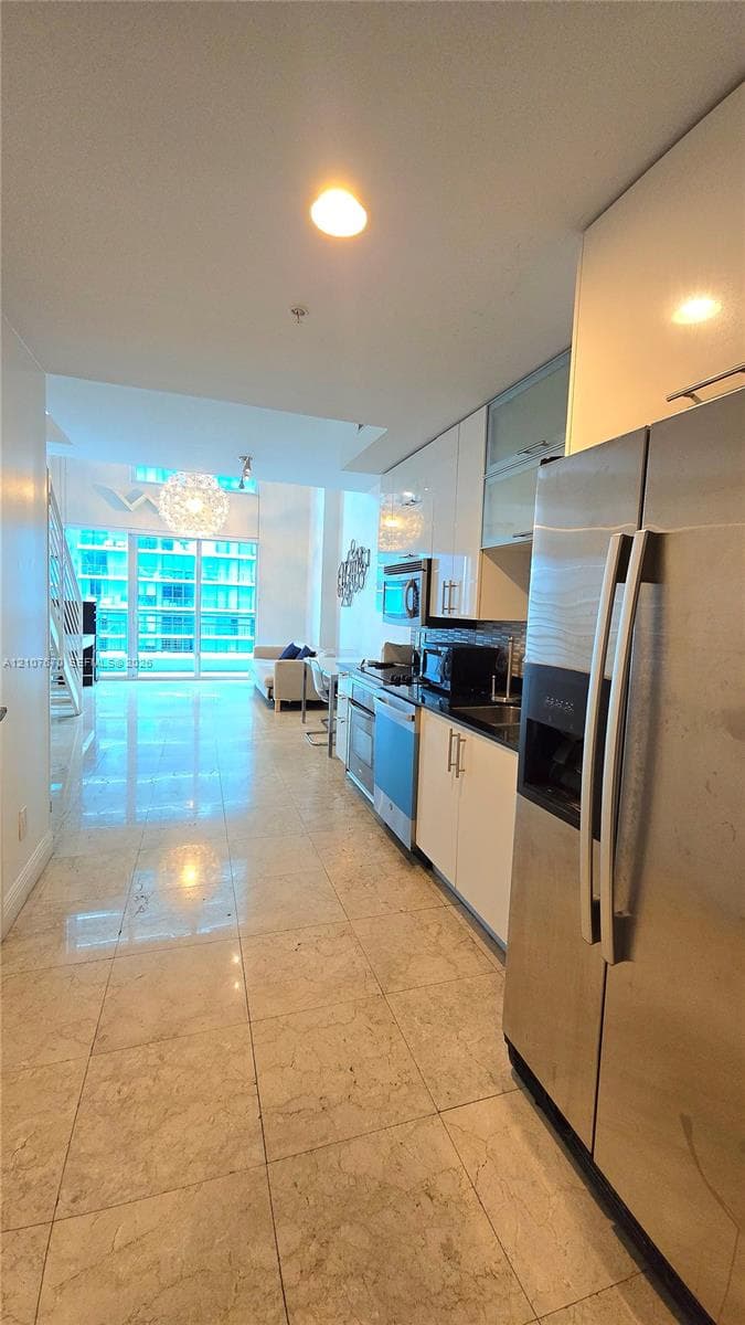 Kitchen featuring high-gloss cabinetry, stainless steel appliances, and stone tile flooring