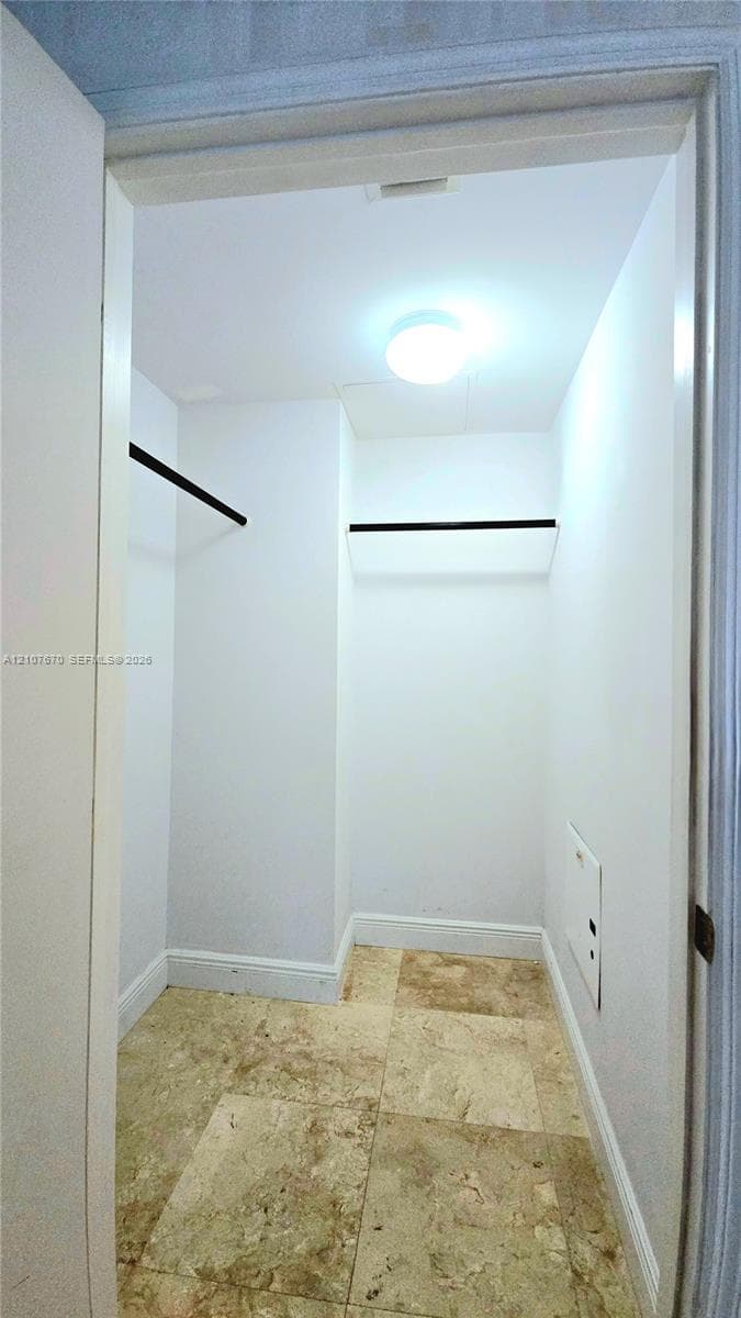 Storage area featuring large-format natural stone flooring, ceiling-mounted lighting, and built-in matte black garment rods