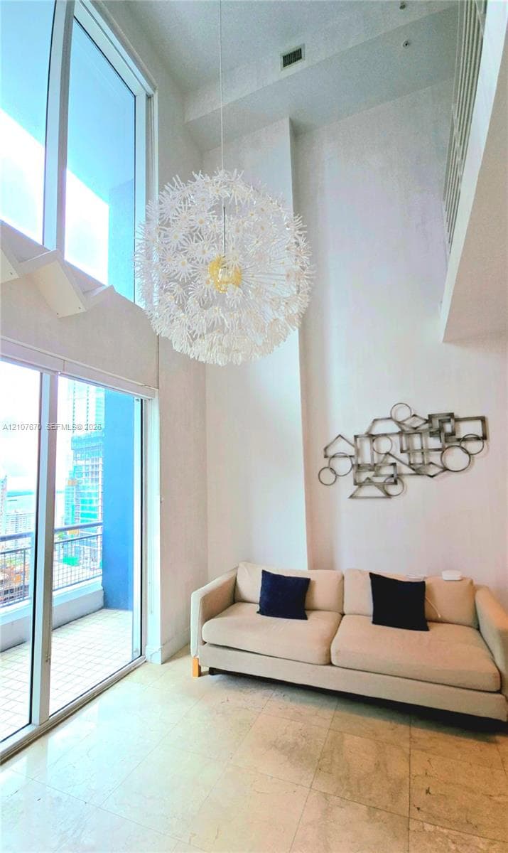 Double-height ceilings featuring floor-to-ceiling windows, polished stone flooring, and a decorative orb pendant light fixture