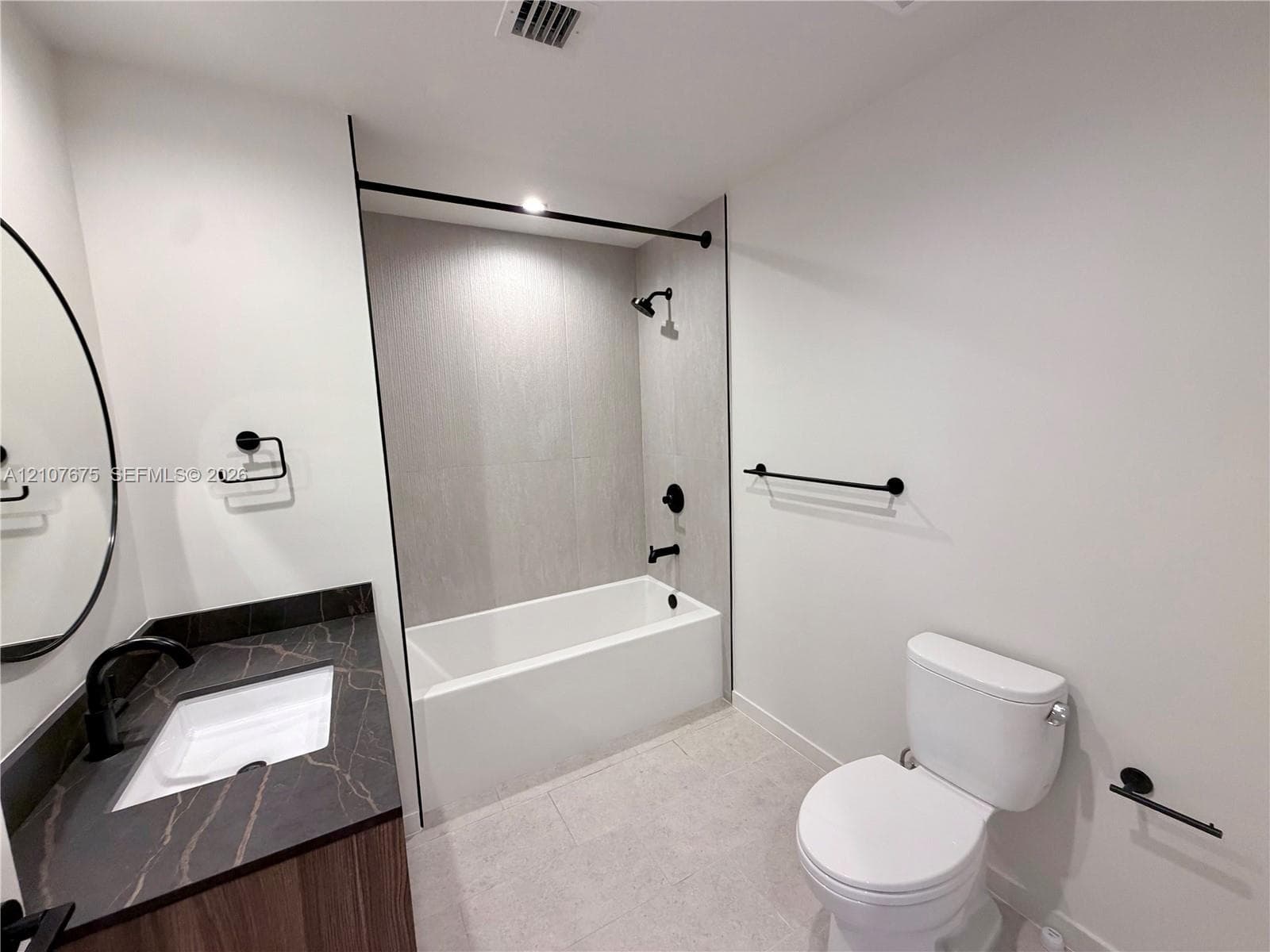 Bathroom featuring a vanity with dark stone-patterned countertop, integrated sink, wood-finish cabinetry, matte black plumbing fixtures, and a tub-shower combination with floor-to-ceiling tile surround