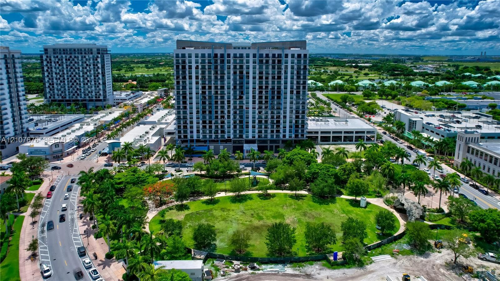 High-rise residential building featuring a glass and concrete facade, integrated parking structure, and extensive green space with established landscaping