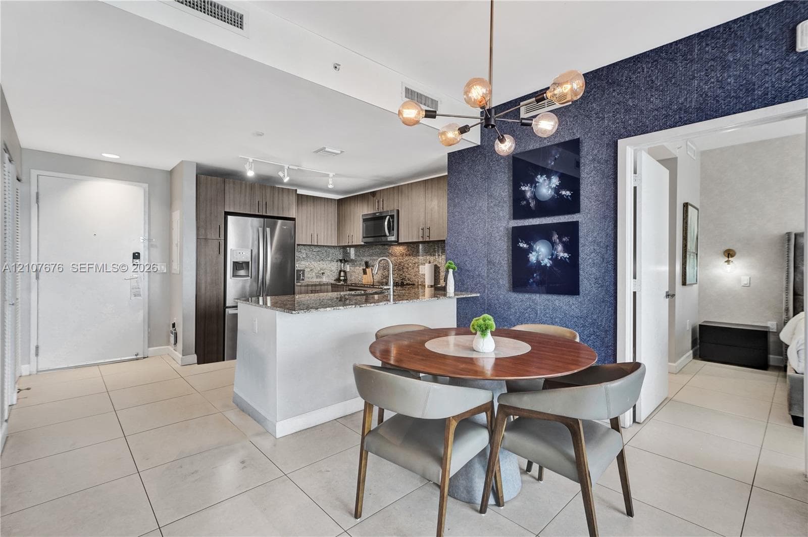 Kitchen featuring stainless steel appliances, stone countertops, and wood-finish cabinetry, complemented by a multi-bulb modern chandelier and a textured accent wall