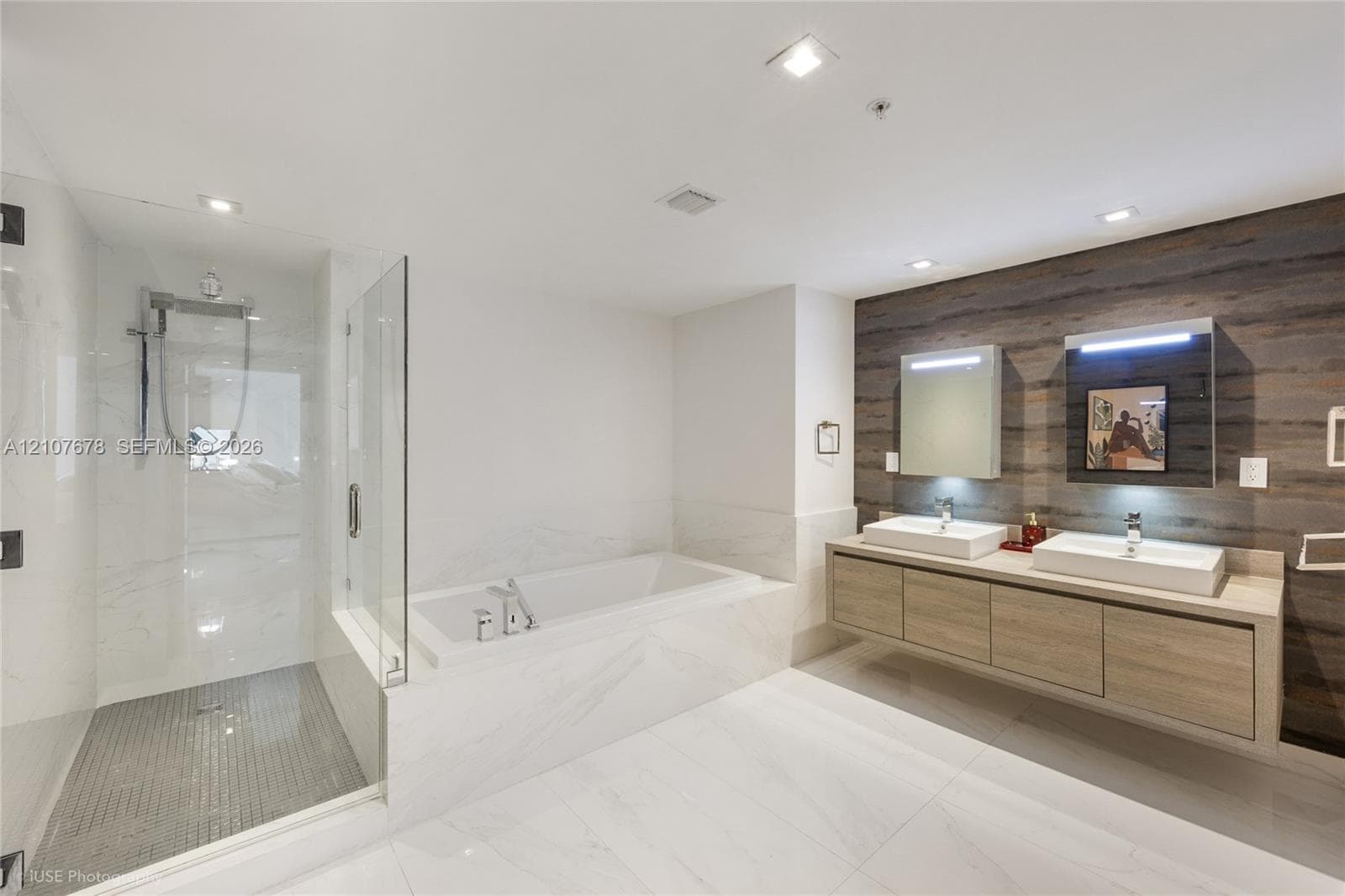 Floating dual-sink vanity with countertop, wood-finish wall paneling, glass-enclosed walk-in shower with tile flooring, and integrated soaking tub featuring stone-finish surrounds