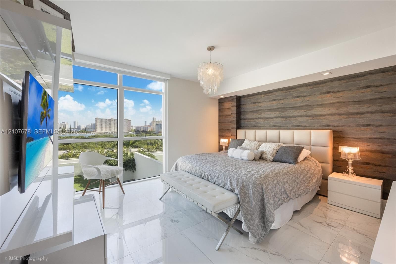 Floor-to-ceiling windows, wood-panel accent wall, polished stone-finish flooring, and decorative chandelier