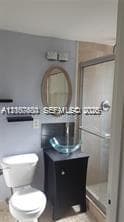 Bathroom featuring a dark wood vanity with a glass vessel sink, oval wall-mounted mirror, two floating wall shelves, and a walk-in shower with a glass enclosure