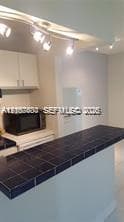 Kitchen featuring a dark tile-surfaced breakfast bar, white cabinetry, track lighting, and a built-in microwave