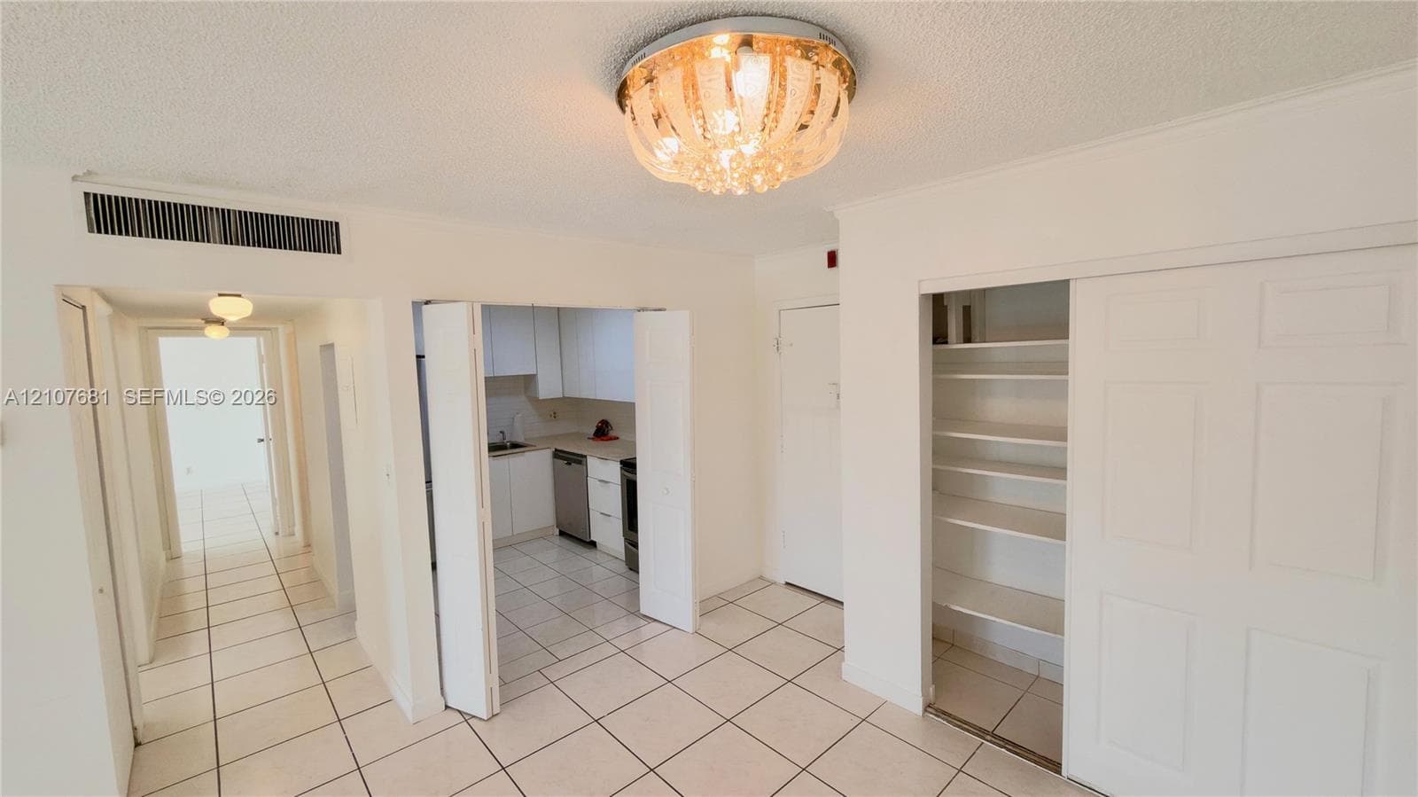 Interior space featuring polished ceramic tile flooring, built-in recessed pantry cabinetry with folding doors, and a decorative flush-mount ceiling light fixture